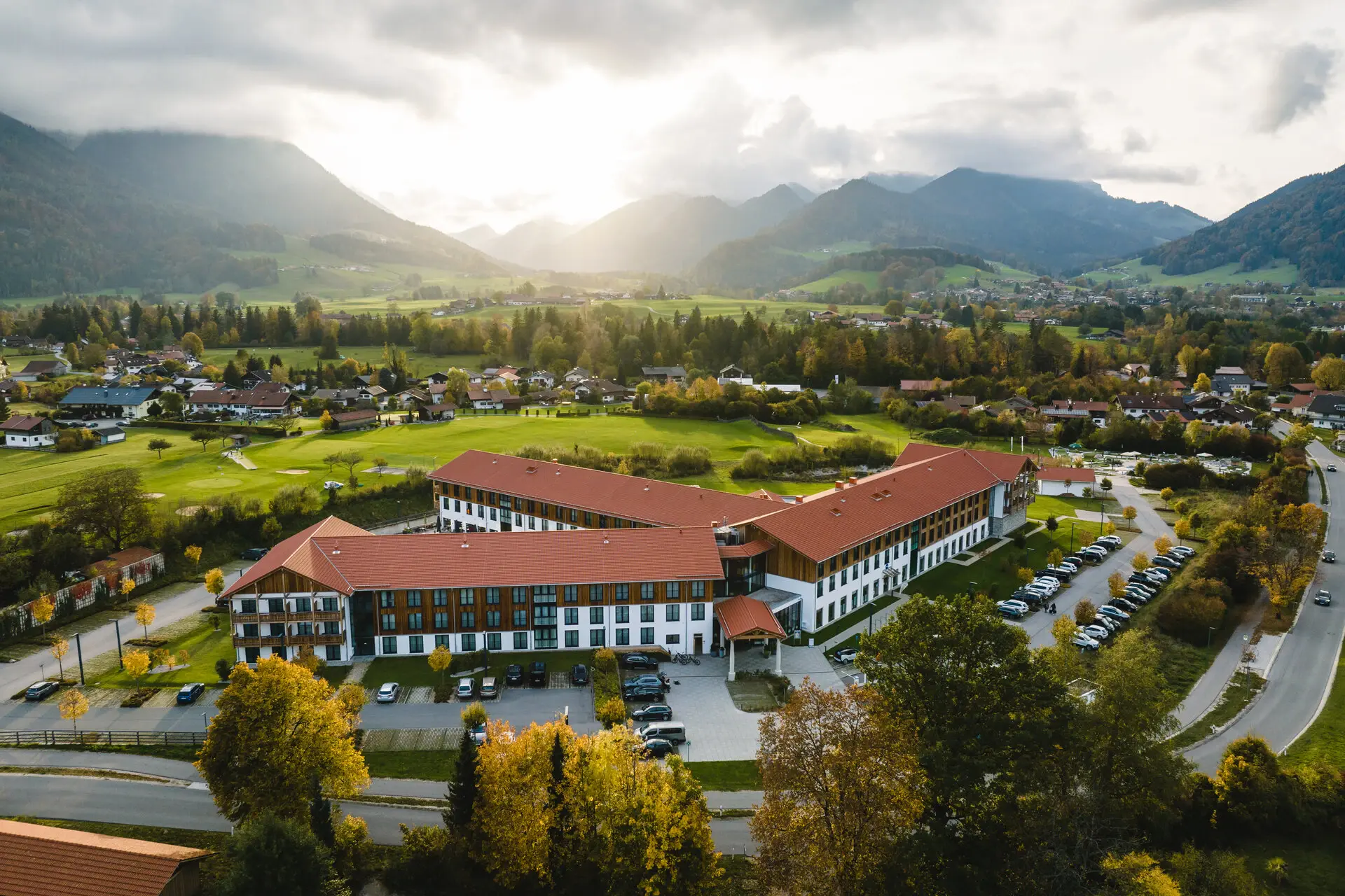 Eine Luftansicht des aja Ruhpolding umgeben von weiteren Häusern, Wäldern und Bergen.