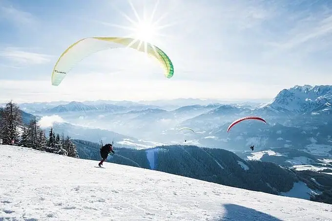 Gruppe von Personen beim Paragliden auf einem verschneiten Berg.