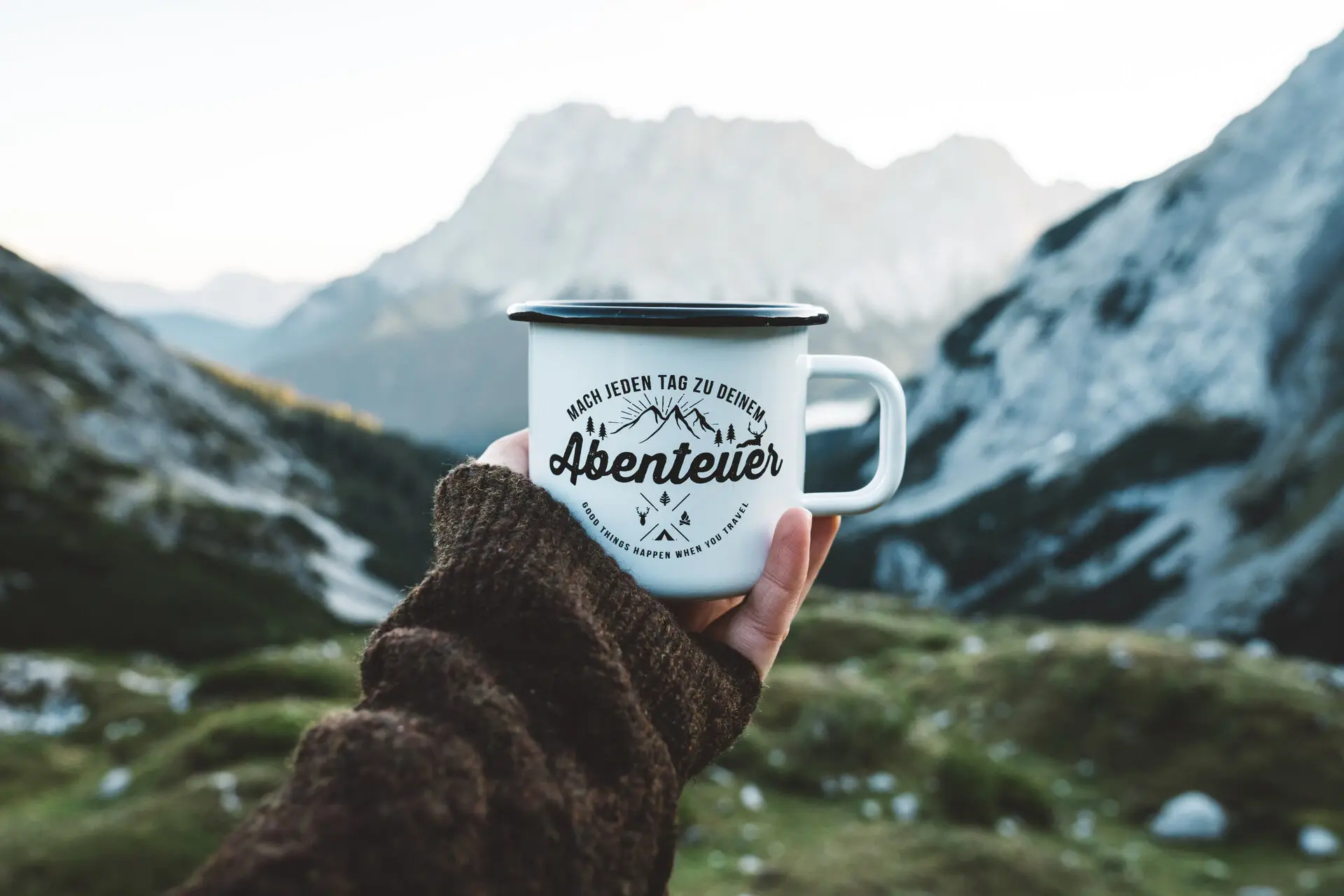 Bergabenteur Eine Person hält eine Tasse vor schneebedeckten Bergen.