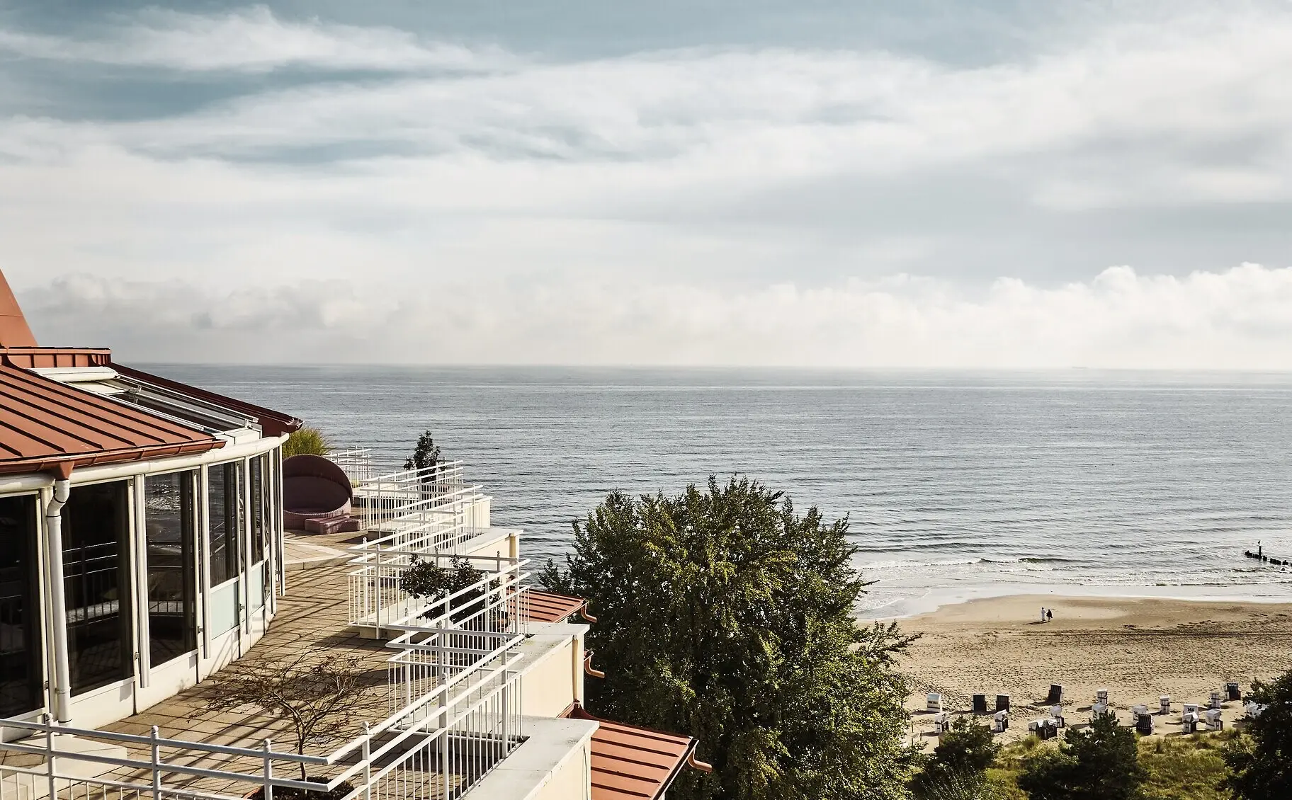 An einem Strand stehen viele weiße Strandkörbe und im Hintergrund ist das aja Bansin zu sehen.