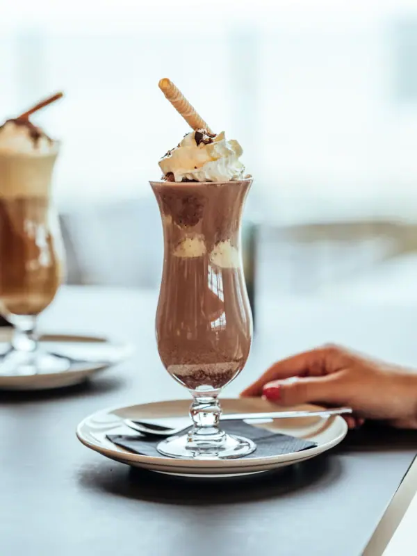 Ein Glas Schokoladenmilchshake mit Schlagsahne und Waffeln.