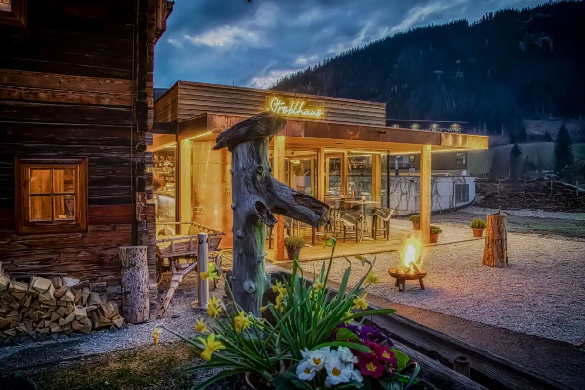 Das Gebäude von vorne mit einer Feuerstelle und einem Baumstumpf davor.