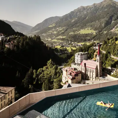 Urban Nature Bad Gastein Eine Person auf einer gelben Luftmatratze in einem Pool mit einem großen Gebäude im Hintergrund.