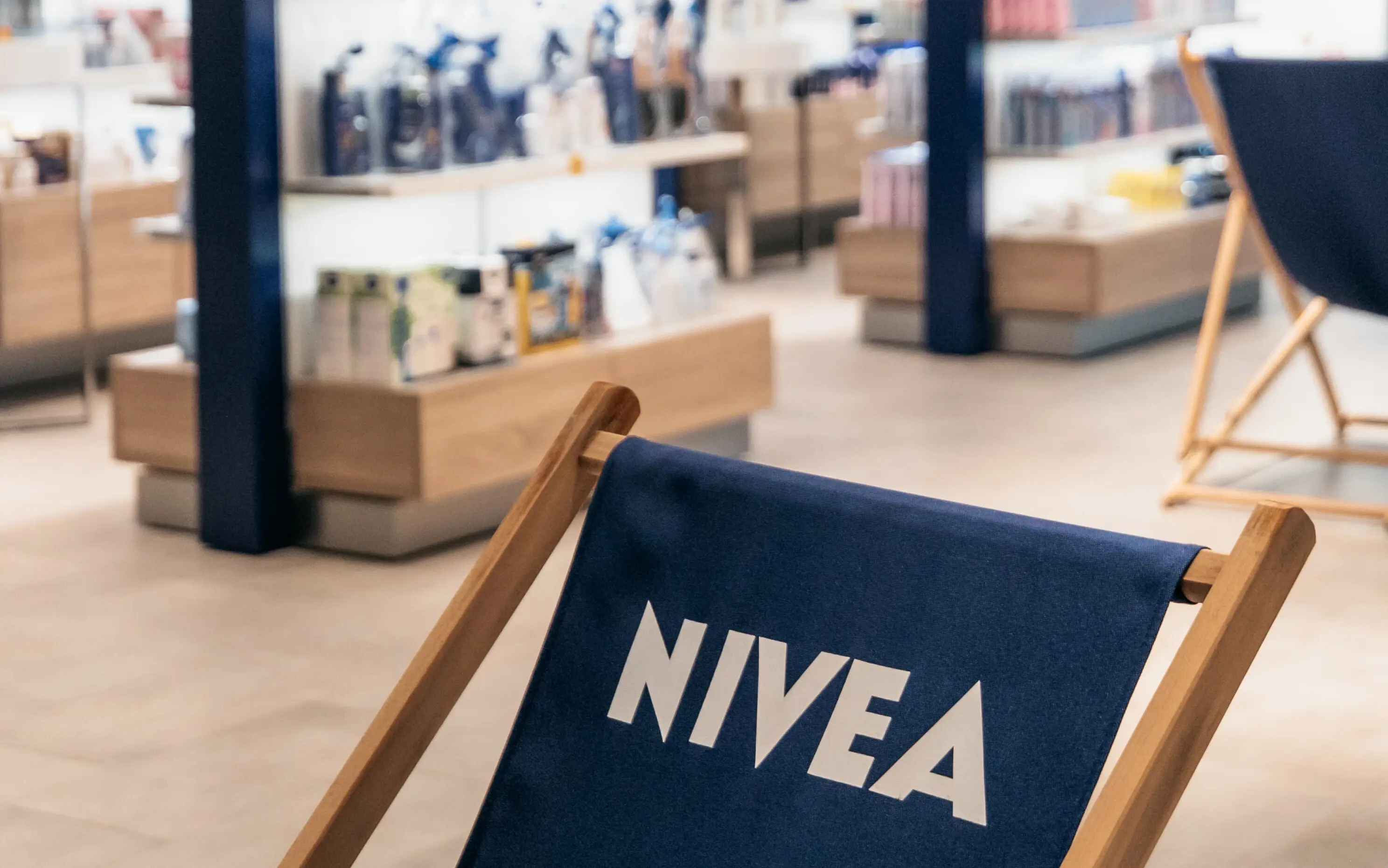 In einem Verkaufsraum mit anthrazitfarbenen Fließen und weißen und dunkelblauen Wänden sind diverse NIVEA Produkte in den Regalen und verschiedenen Verkaufsaufstellern zu erkennen.