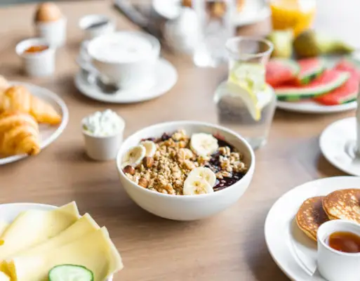 Frühstück Eine Schale Müsli mit Bananen und Pfannkuchen auf einem Tisch.