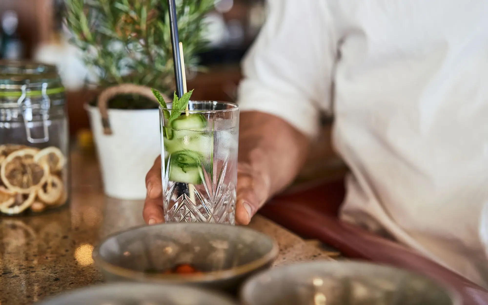 Ein Mann hält ein Longdrinkglas auf einer Bartheke.