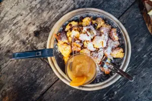 Auf einem Holztisch steht eine Puderzucker überstreute Pfanne Kaiserschmarren. 