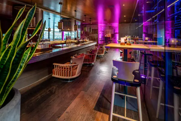 Eine Bar mit Stühlen und Tischen in einem Raum mit violetten Lichtern.