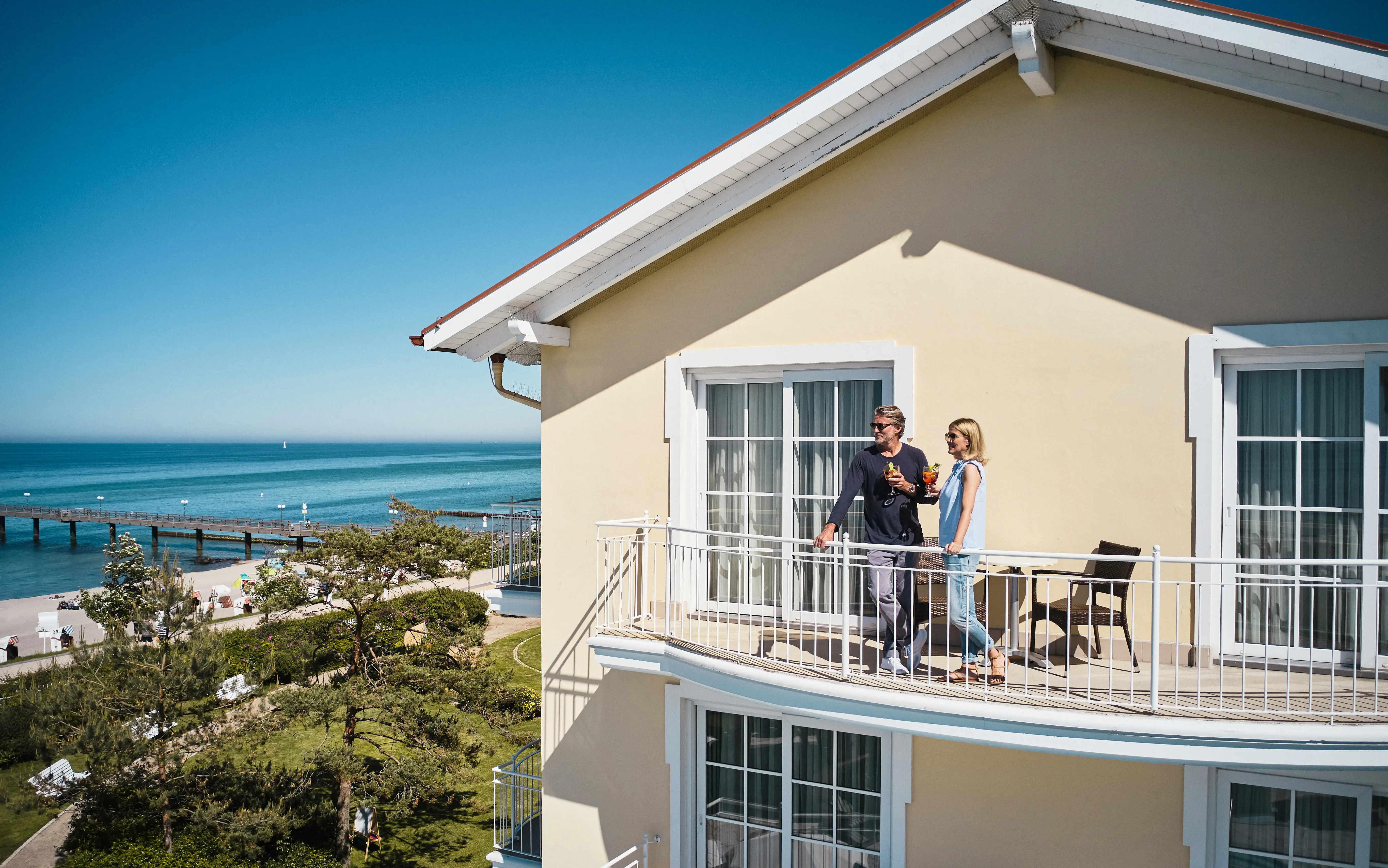 Mann und Frau stehen auf einem Balkon mit Blick auf einen Strand.