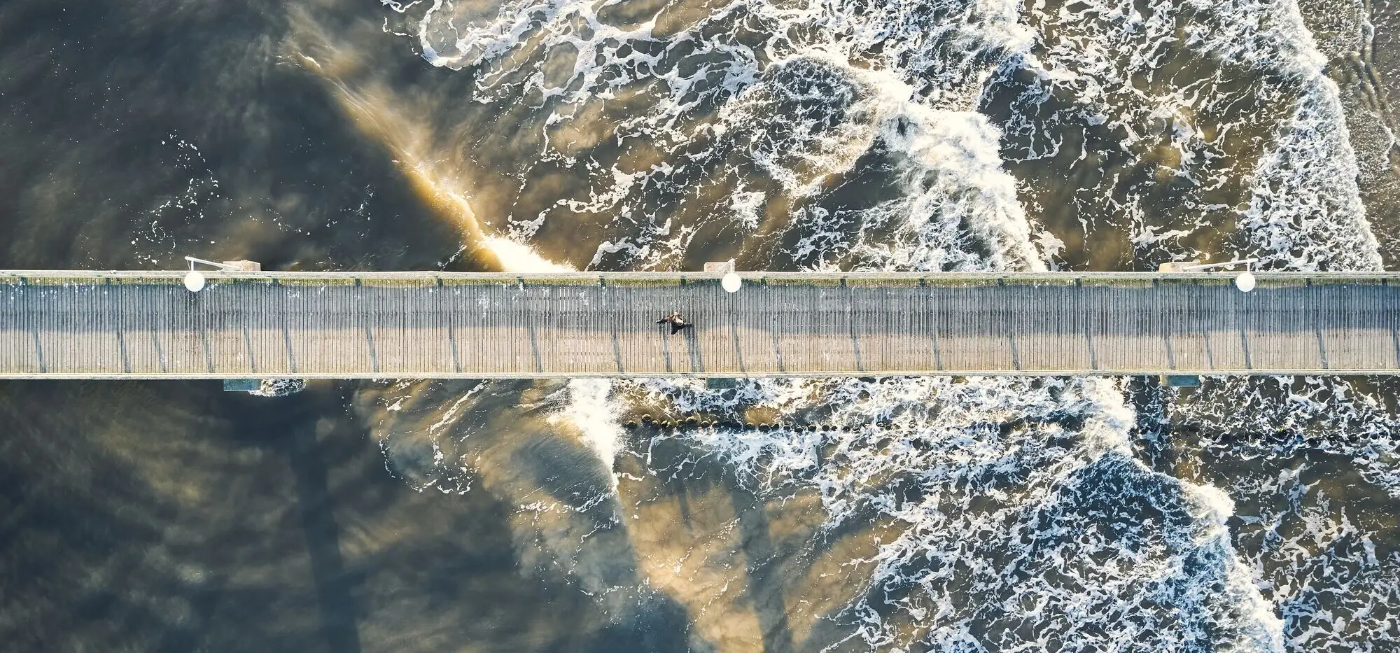 Eine Seebrücke aus der Vogelperspektive mit einer Person darauf.