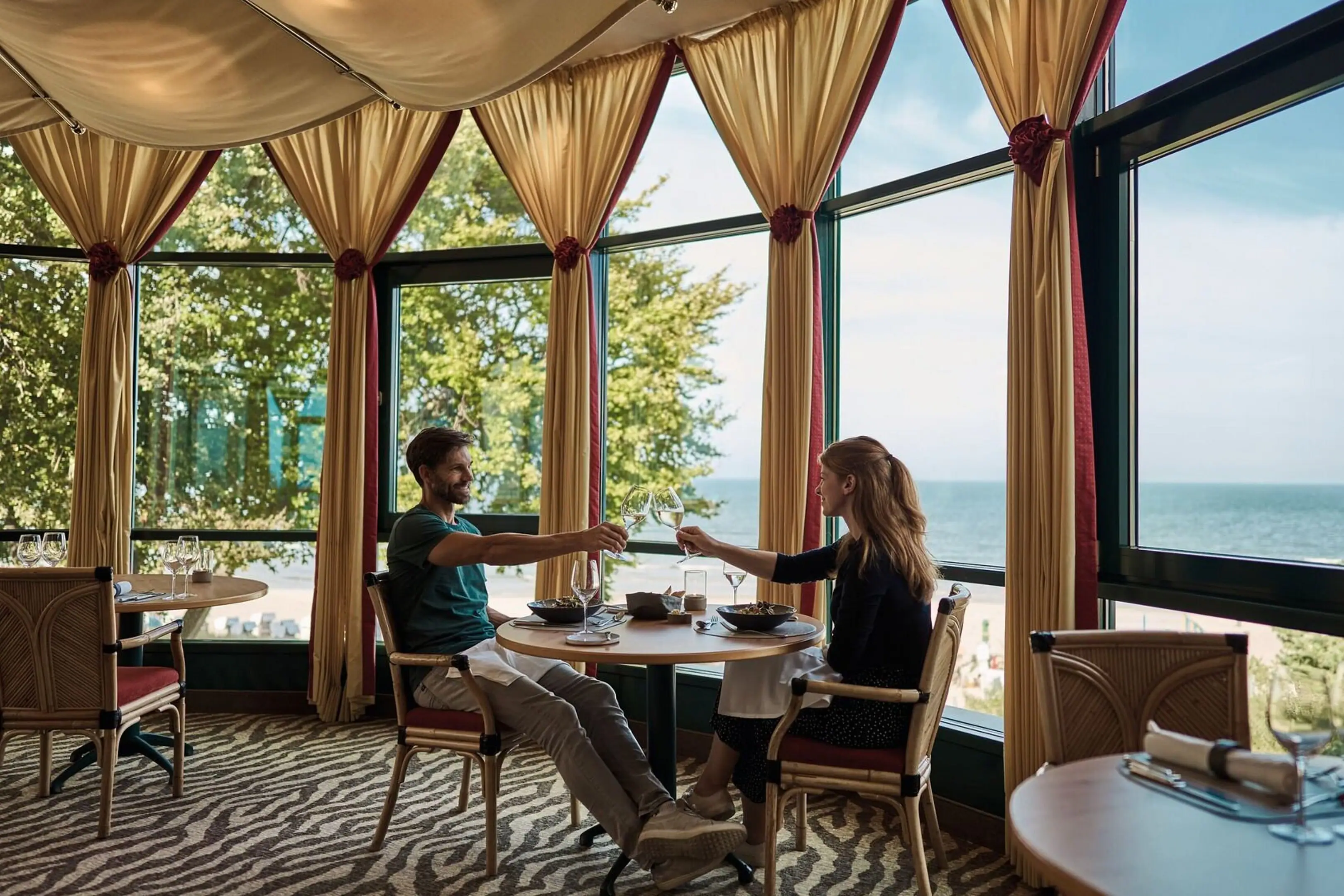 Ein Mann und eine Frau sitzen an einem Tisch mit Essen vor einem großen Fenster.