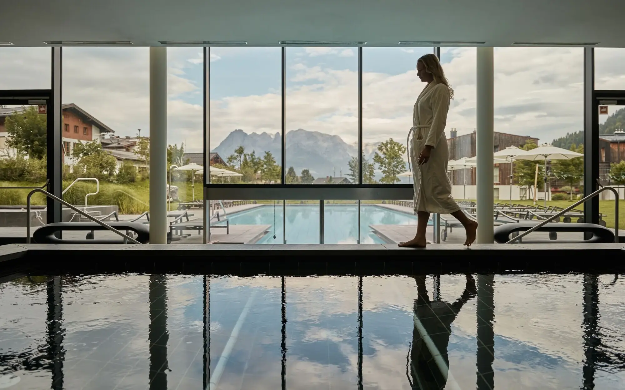 Frau geht an einem Pool vorbei, Spiegelung im Wasser.