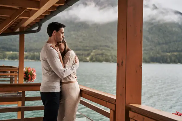 Ein Mann und eine Frau umarmen sich auf einer Veranda mit Blick auf einen See.