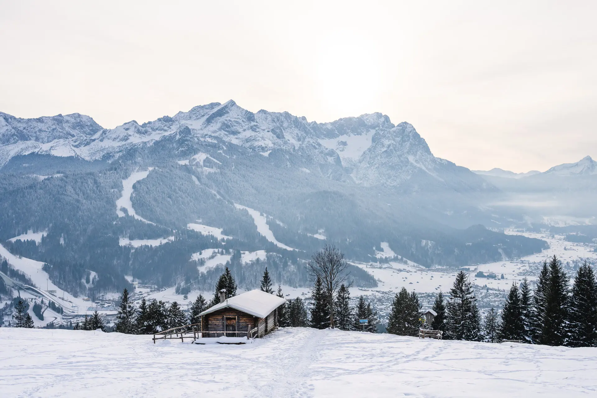 Eine Hütte im verschneiten Wald mit sichtbaren Bergen im Hintergrund.