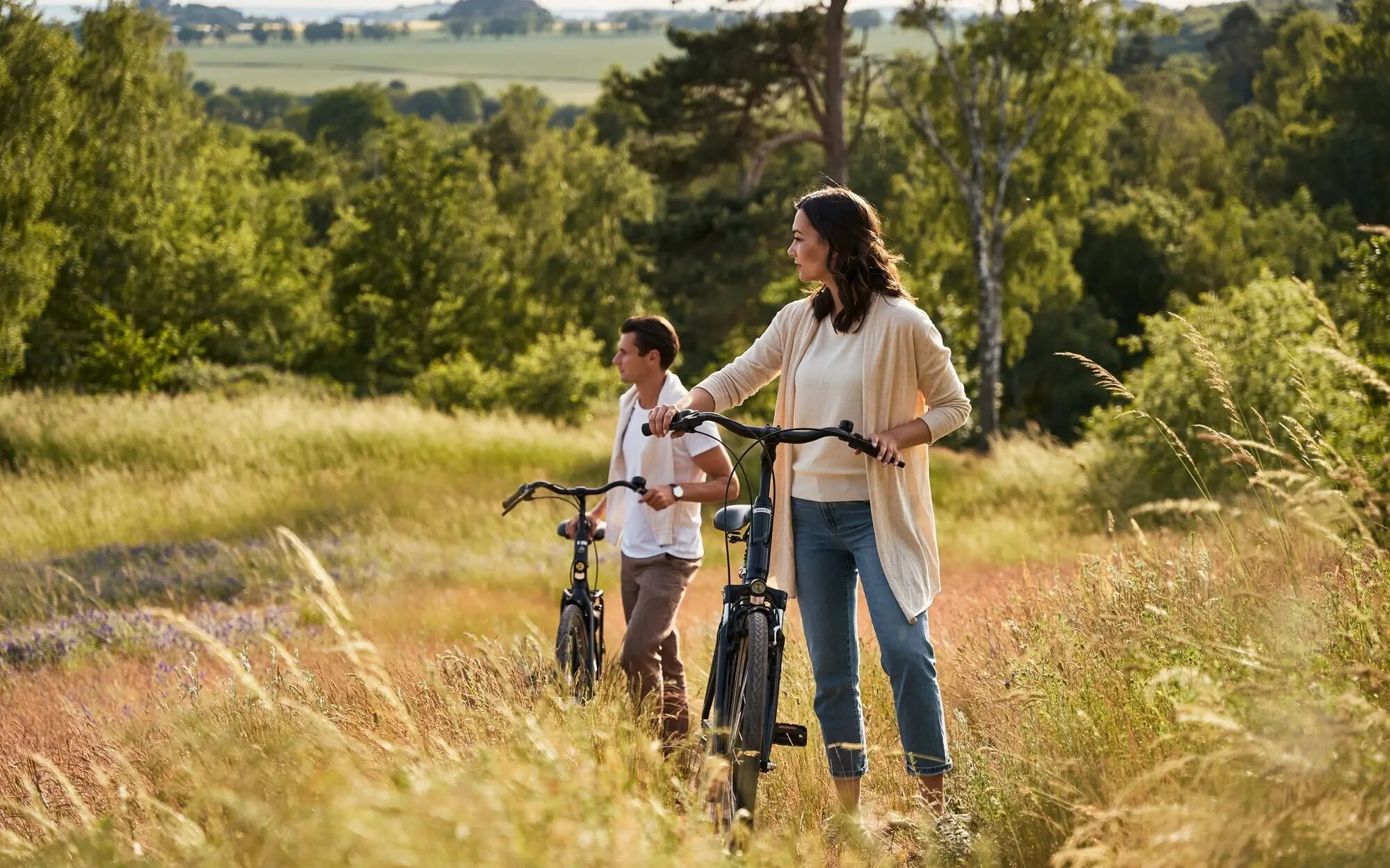 Paar mit Fahrrädern steht inmitten einer sommerlichen Wiesenlandschaft auf Rügen; sie genießen den Ausblick über die hügelige Natur und blühende Felder unter freiem Himmel.