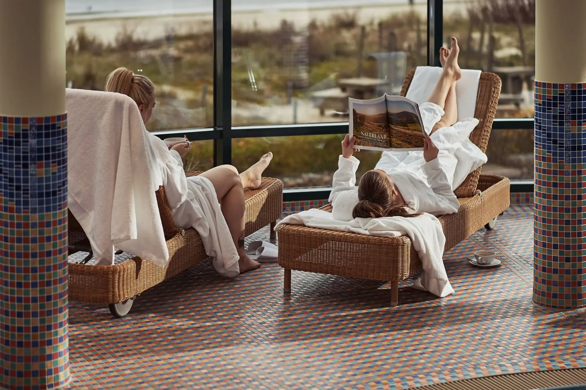 Zwei Frauen in weißen Bademänteln liegen auf Stühlen.