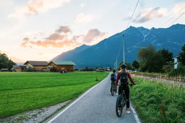 Radfahren Menschen auf Fahrrädern auf einer Straße mit Gras und Bergen im Hintergrund.