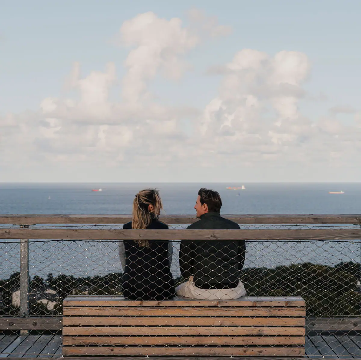 Ein Mann und eine Frau sitzen auf einer Bank mit Blick auf das Meer.
