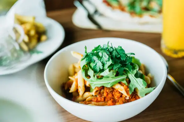 Linsenbolognese Eine Schüssel Pasta mit Sauce und grünen Zutaten.
