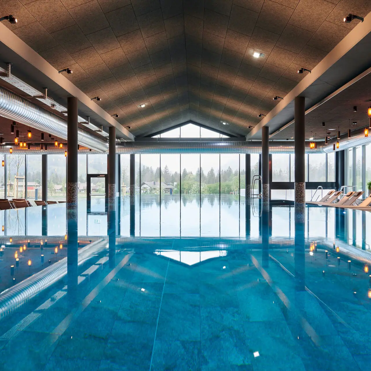 Innenpool im aja Ruhpolding Großes Hallenbad mit hohen Decken und großen Fenstern.