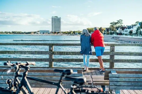 Paar am Meer Ein Mann und eine Frau stehen auf einer Holzbrücke und blicken auf das Wasser.