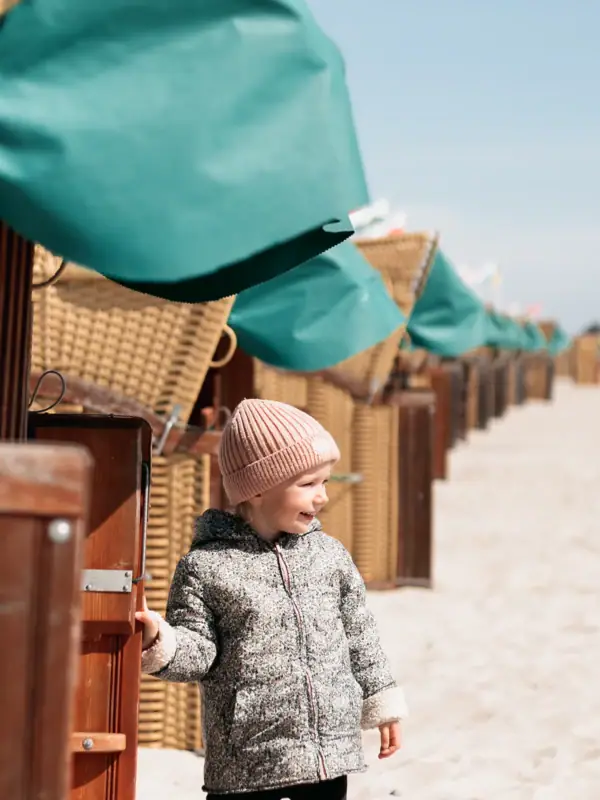 Kind vorm Strandkorb Ein Kind steht im Sand neben einer Reihe von Strandhütten.