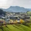 Eine Stadt mit vielen Gebäuden, umgeben von grünen Wiesen und Bergen im Hintergrund.