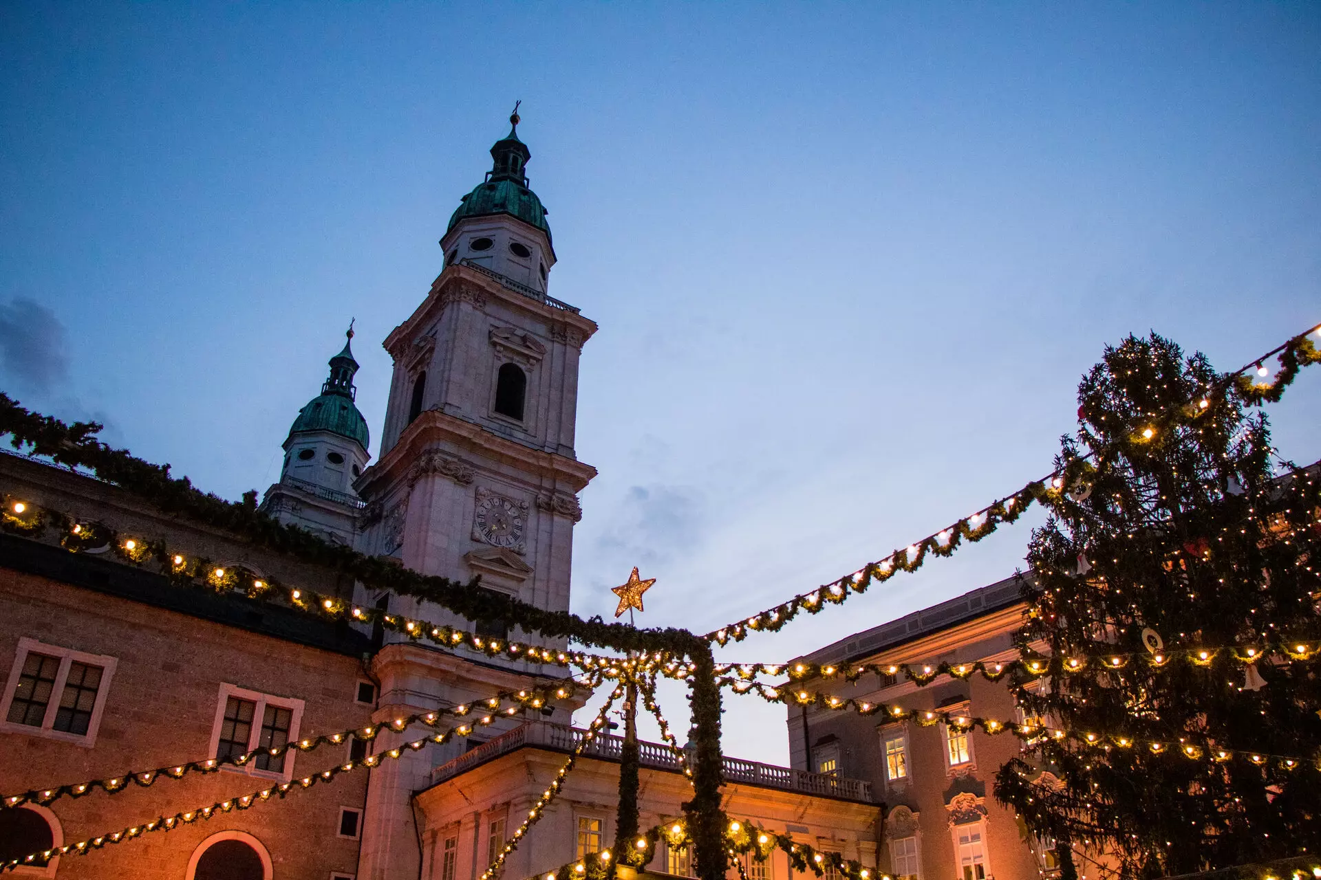 Beleuchtetes Gebäude mit Turm und Uhr, umgeben von Bäumen, bei Nacht.