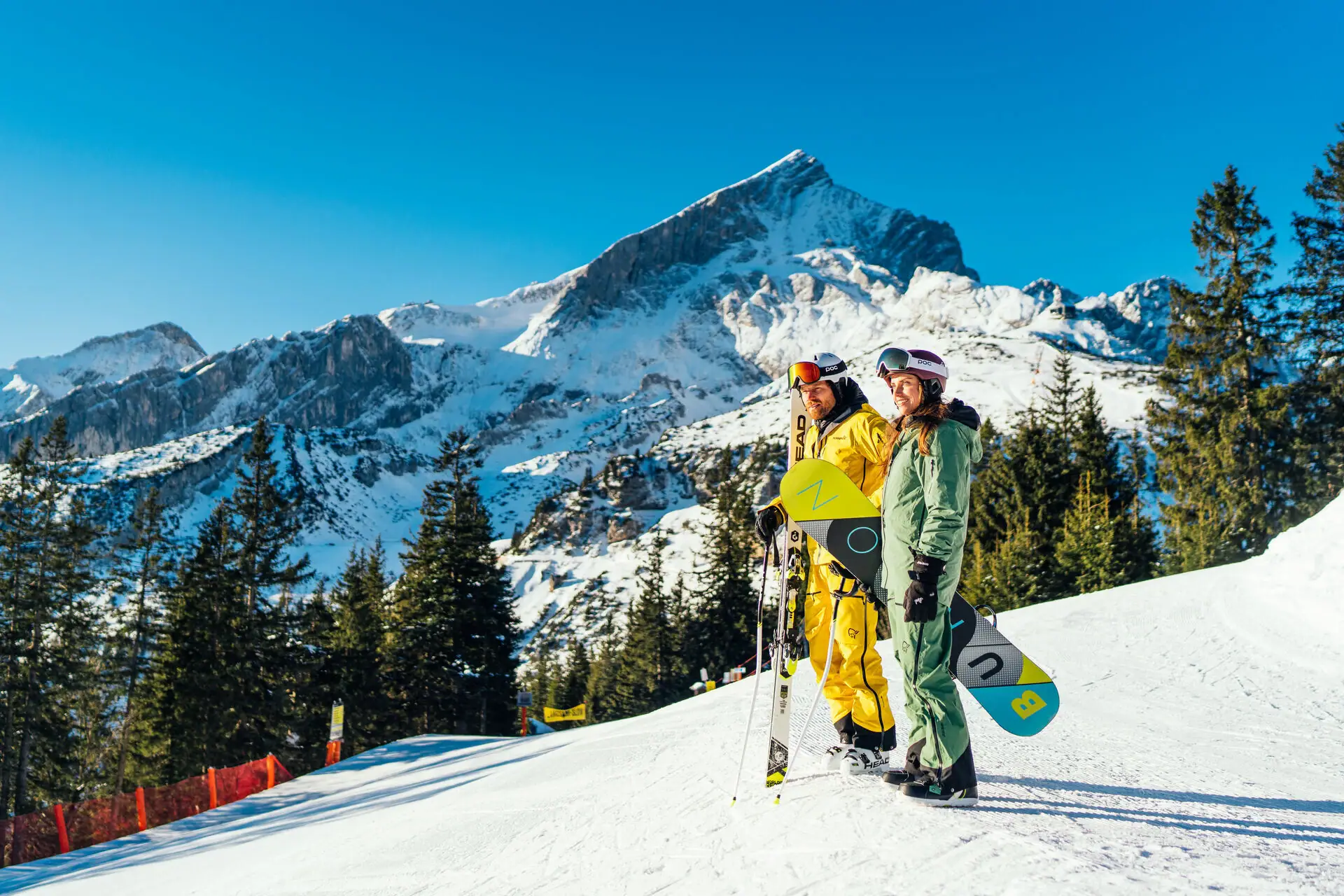 Zwei Personen in Schneekleidung stehen auf einem verschneiten Berg.