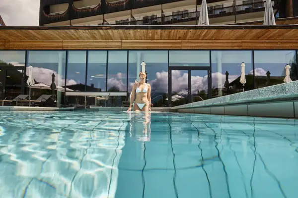 Badewelt im aja Bergresort Werfenweng Eine Frau in einem Schwimmbecken mit dem Hotel im Hintergrund.