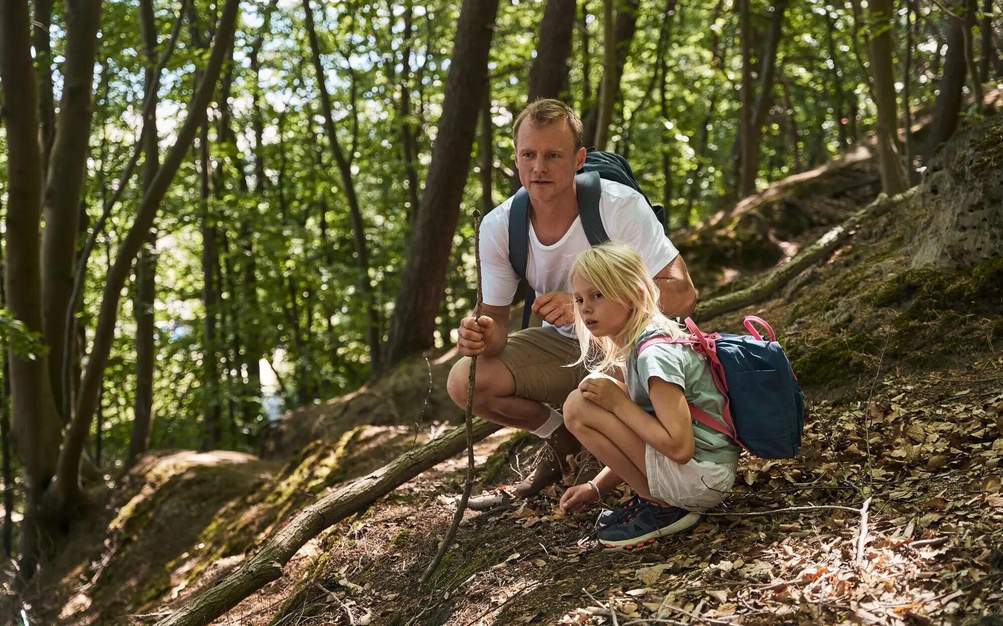 A man and a girl are sitting on a hill in the forest.