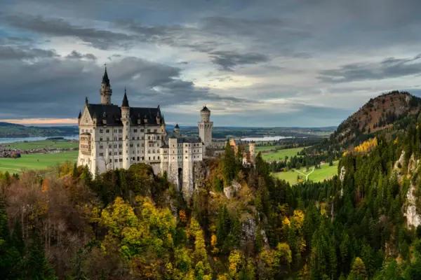 Schloss Neuschwanstein auf einem Hügel mit Bergen im Hintergrund.