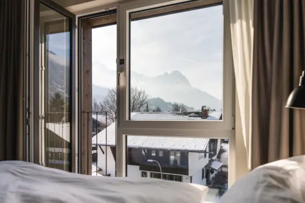 Ein Hotelzimmer im aja Garmisch-Partenkirchen mit Fenster und Blick auf die Berge.