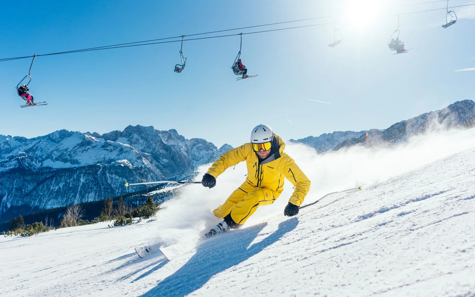 Person beim Skifahren in einem gelben Skianzug auf einem verschneiten Berghang.