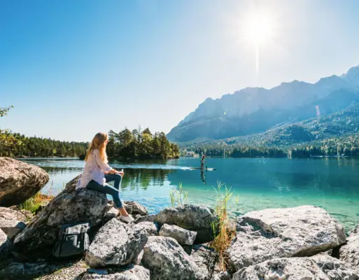Eine Frau sitzt auf einem Felsen am See.