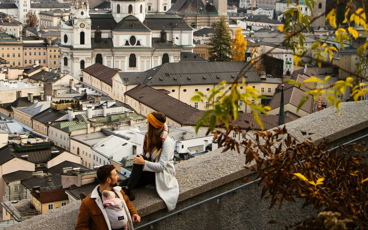 Ein Mann und eine Frau stehen bei einer Mauer leicht erhöht und überblicken Salzburg an einem Herbsttag. 