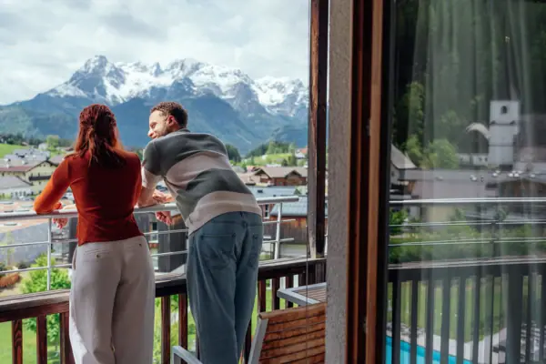 Ein Mann und eine Frau stehen auf einem Balkon und blicken auf Berge.