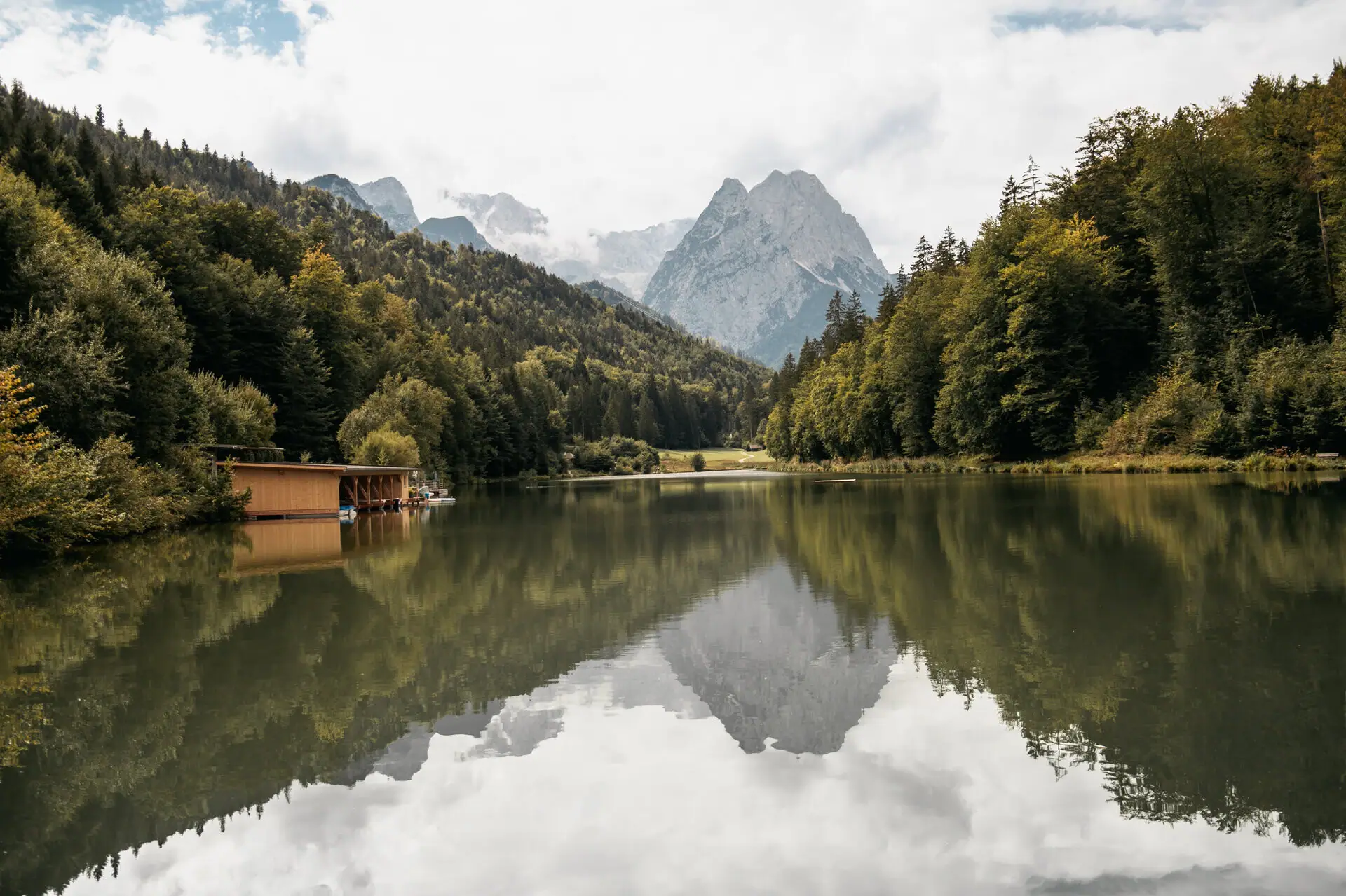 Ein See mit einer Hütte und Bergen im Hintergrund.
