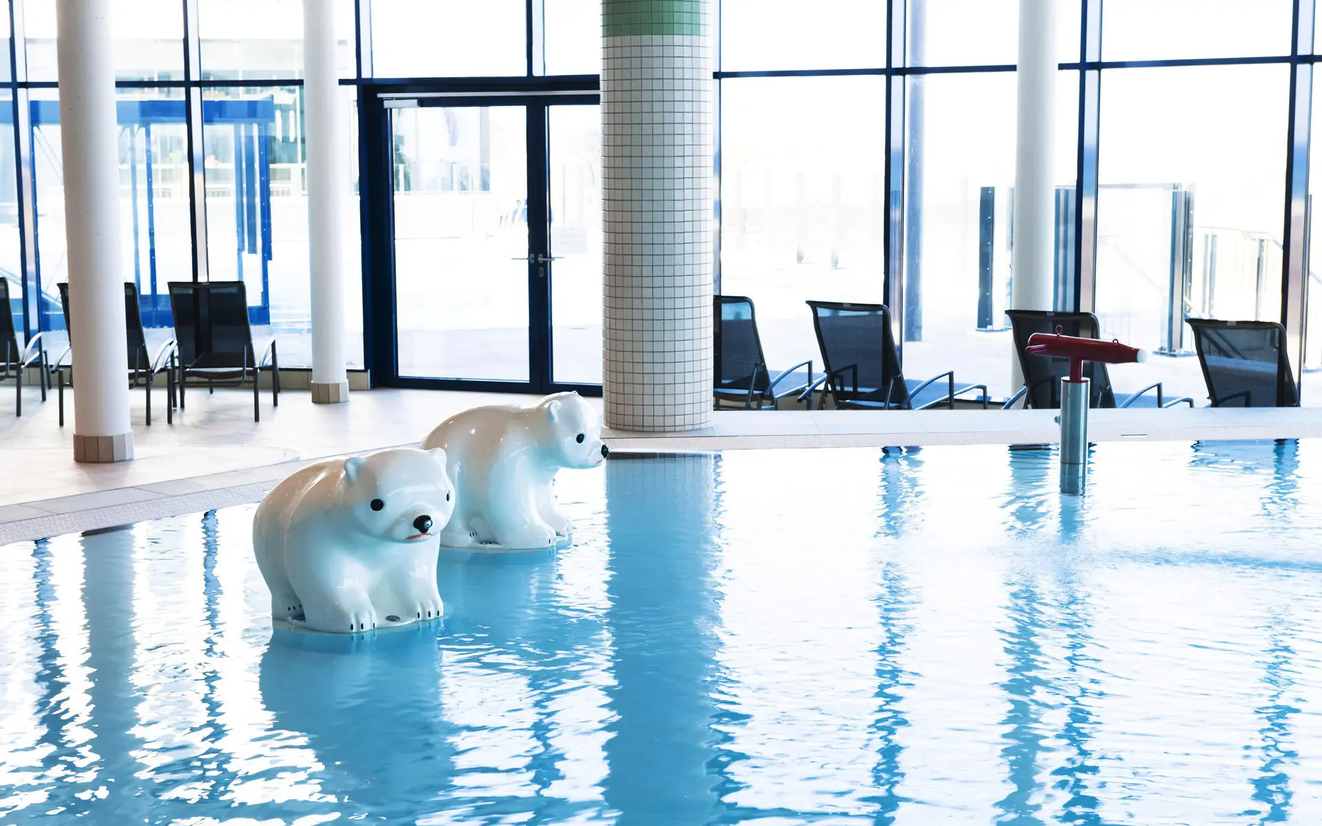 Ein Kinderbecken im Schwimmbereich mit zwei Eisbärfiguren. Im Hintergrund stehen Liegen, ausgerichtet mit dem Blick nach draußen auf den Außenpool.