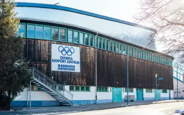 Olympia-Eissport-Zentrum Garmisch-Partenkirchen, umgeben von Bäumen und blauem Himmel.