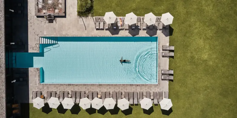 Bird's eye view of a pool surrounded by parasols and grass.