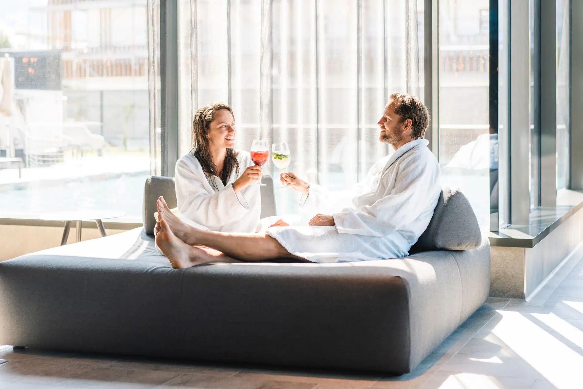 Drinks am Pool Ein Mann und eine Frau in Bademänteln sitzen auf einem Sofa.