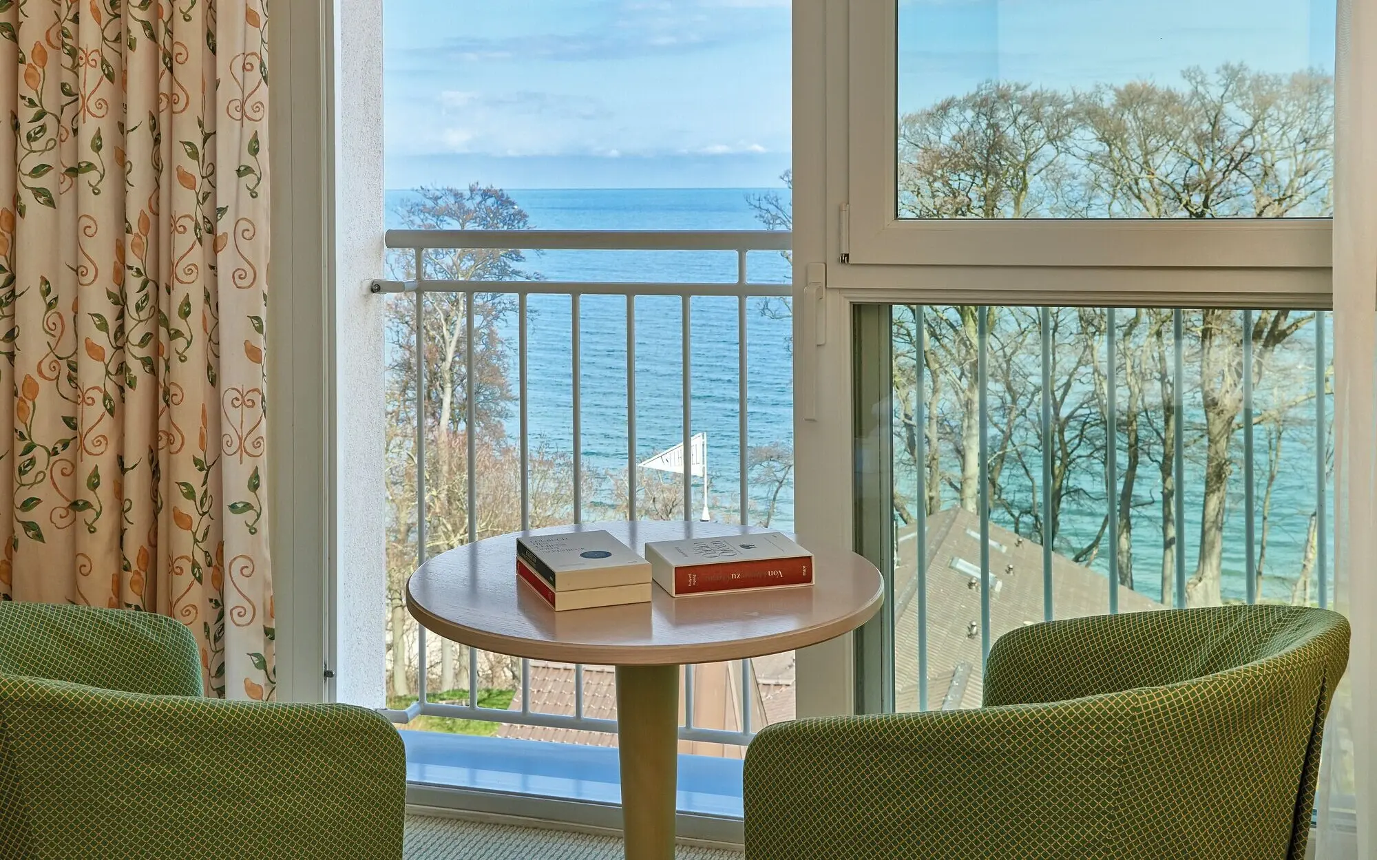 Ein Tisch mit Büchern darauf vor einem Balkon mit Blick auf das Meer.