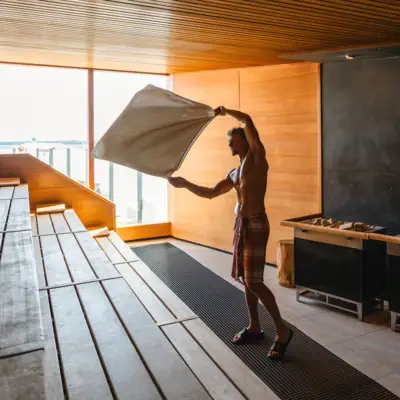 Sauna im aja Travemünde Ein Mann hält ein Handtuch in einer Sauna und gibt einen Saunaaufguss.