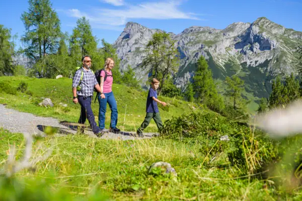 Wanderung Eine Gruppe von Menschen wandert auf einem Pfad in einer grasbewachsenen Gegend mit Bergen im Hintergrund.