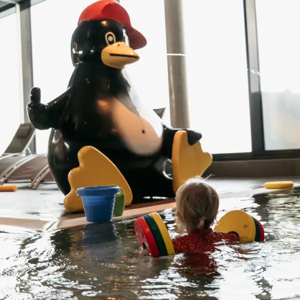 Ein Kind schwimmt in einem Pool neben einer Pinguin-Statue.