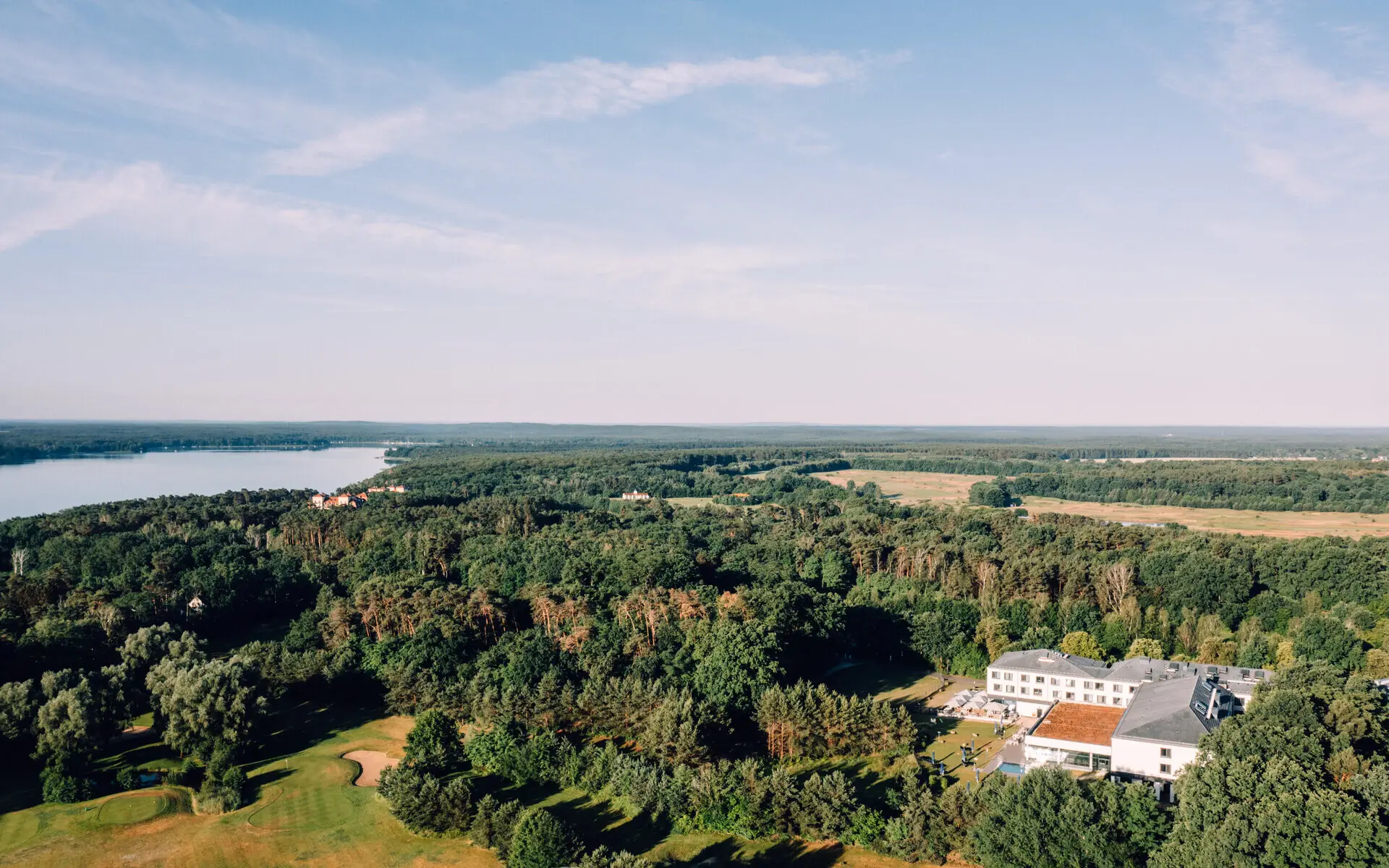 Luftansicht des aja Bad Saarow, der umliegenden Wälder und des Sees im Hintergrund. 