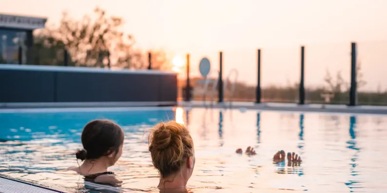 Zwei Frauen schwimmen bei Sonnenuntergang in einem ruhigen Außenpool.