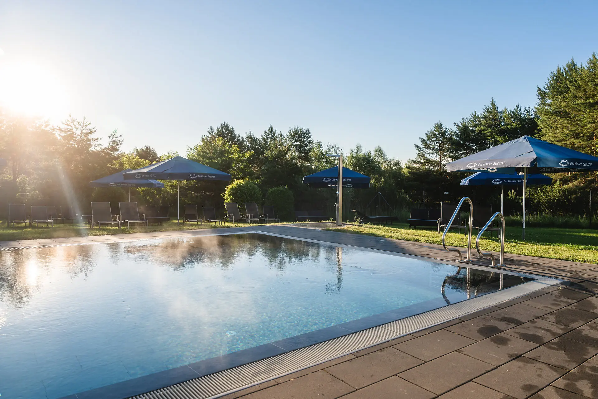 Ein Pool mit Sonnenschirmen und Rasen.
