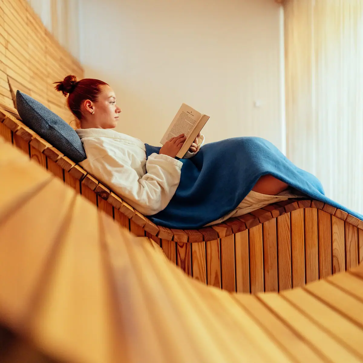 SPA-Liege Eine Frau liest ein Buch auf einer Holzbank.